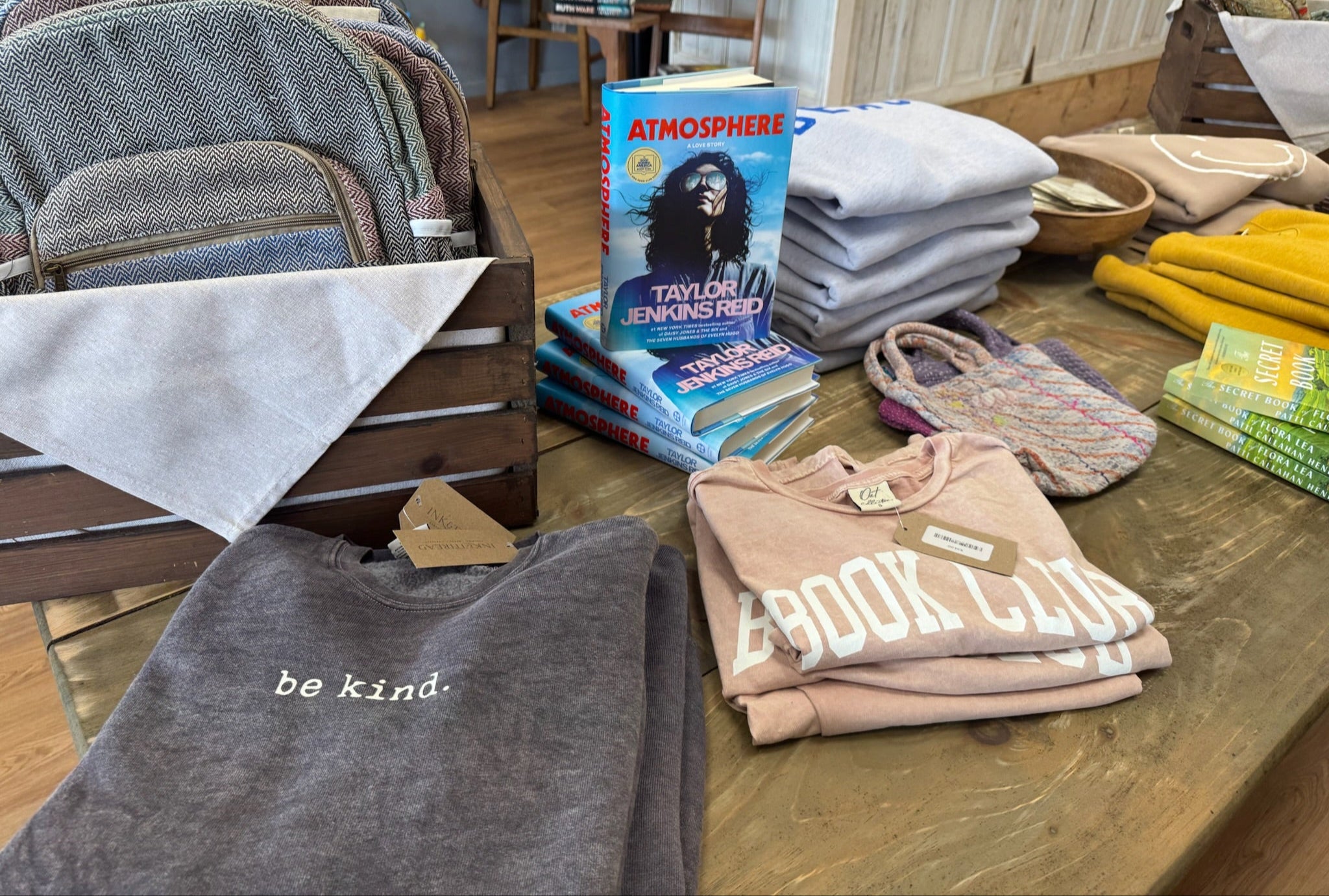 Stacks of books, shirts, and bags on a wooden table with a casual setting.